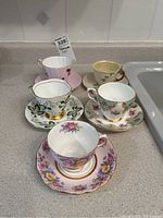 Five vintage teacups and saucers displayed on a kitchen counter, showing floral and gold trim details.