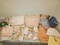 Photo showing a variety of baby doll clothing items, linens, blankets, gloves, and shoes in pastel colors laid out on a surface