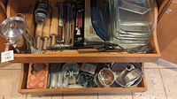 Overview of two drawers containing baking pans, molds, rolling pins, grilling utensils, glass baking dishes, and other kitchen tools.