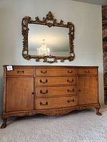 Full front view of wood buffet with ornate mirror mounted above on wall