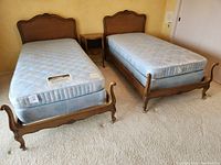 Two carved wood twin bed frames each fitted with pale blue floral-patterned mattresses and box springs on brass casters