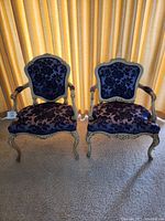 Pair of blue velvet upholstered armchairs with carved wooden frames, positioned side by side on carpet in front of yellow curtains.