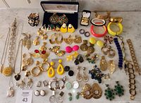 Overhead view of entire lot on marble surface showing necklaces, bracelets, bangles, and numerous pairs of earrings