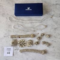 Wide view of all jewelry pieces including necklaces, bracelets, brooches and earrings on marble surface with Swarovski box