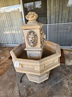 Front perspective of carved lion fountain with octagonal basin, decorative urn top, visible power cord