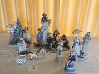 Group of porcelain figurines including three Lladró pieces and assorted Nadal urns and animals on cloth background.
