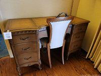 Corner view of wooden office desk with multiple drawers and upholstered office chair pulled under desk