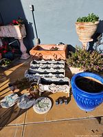 Wide view of lot showing wrought iron planters stacked, large rectangular terracotta planter, blue glazed pot, succulents, and garden stepping stones
