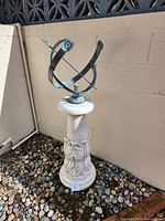 Full view of patinated metal sundial mounted on plaster pedestal