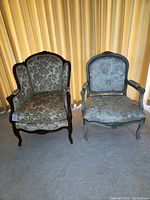 Front view of two armless chairs side by side, showing upholstery and carved wooden frames.