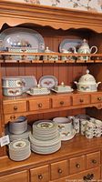 Wooden hutch displaying top and middle shelves with serving platters, covered dishes, tureen and place settings on lower shelf