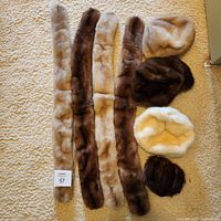Four long mink scarves laid out on carpet with four fur hats at right
