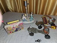 Photo showing a lamp with wooden figurines, adjustable metal roller skates with leather straps, and a boxed toy cookware set with a yellow toy resembling a banana.