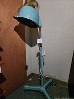 Full standing view of vintage hairdryer with light blue dome and chrome accents, cord wrapped around pole.