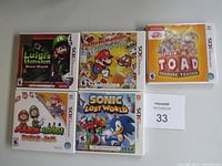 Photo showing five Nintendo 3DS game cases including Luigi's Mansion: Dark Moon, Paper Mario, Captain Toad: Treasure Tracker, Mario & Luigi: Paper Jam, and Sonic Lost World arranged on a flat surface.
