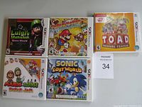 Five sealed Nintendo 3DS game boxes arranged in two rows: Luigi’s Mansion: Dark Moon, Paper Mario: Sticker Star, Captain Toad: Treasure Tracker, Mario & Luigi: Paper Jam, Sonic Lost World.