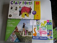 Photo showing the Crazy Forts box with 69 pieces, the Ring Toss set box, and the Balloon Modelling kit box arranged on a surface.