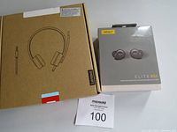 Image of the unopened Lenovo wired headphones box and unopened Jabra Elite 85t earbuds box side by side on a white background with auction tag 100 number visible.