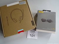 Boxed Lenovo wired headphones and boxed Jabra Elite 85t earbuds placed side by side on a flat surface with auction lot tag visible