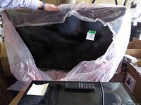 Samsung TV partially covered in protective plastic wrap with remote on subwoofer in front.