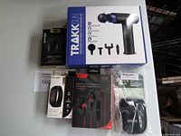 Photo of Trakk professional muscle massager box with image and attachments, Escape sport earbuds, Roots camera case pouch, Maskid fitness tracker box, and other earbuds.