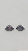 Close-up photo of the pair of trillion cut fancy purple sapphire gemstones side by side on a plain white background.