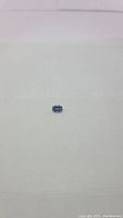 Oval cut natural tanzanite gemstone shown from a distance on a light surface, color appears violet-blue, oval shape visible