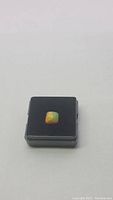 Cushion cut Ethiopian opal in display box showing butterscotch color and rainbow flashes, positioned flat.