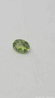 Close-up photo of a natural apple green peridot gemstone showing oval cut and clarity.