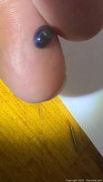 Close-up photos of the natural blue star sapphire cabochon highlighted on the finger under lighting to show the six-rayed star effect.
