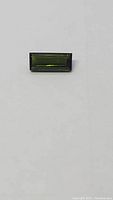 Close-up photos of a bright green baguette cut natural tourmaline gemstone on a light background.