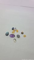 Photo showing 13 assorted natural gemstones of various types arranged on a white surface, including amethyst, caramel opal, labradorite, kyanite, and citrine.