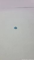 Natural pear cut lagoon blue Swiss blue topaz gemstone lying on white surface, showing top facet view