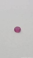 Close-up of oval cut ruby gemstone showing rich pink-red color and polished surface.