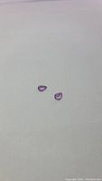 Photo of two natural pear cut purple amethyst gemstones placed on a white surface, showing their size, shape, and color.