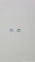 Close-up of the two pear cut sky blue topaz gemstones resting on a white surface showing their shape and color.