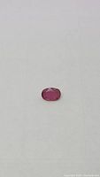Close-up view of the natural pink ruby gemstone showing oval cut and color details against a light background.