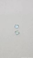 Pair of two pale blue sugarloaf cut aquamarine gemstones on a neutral surface.