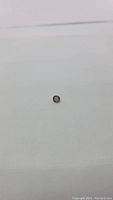 Photo showing small cushion cut spinel gemstone with purple and orange coloration on neutral background.