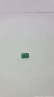 Single natural vivid lime green onyx gemstone, emerald cut, placed on a white background for clarity of cut and color.