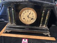 Front view of the black antique mantel clock showing the clock face, green marbleized columns, and ornate metal feet on a wooden base.