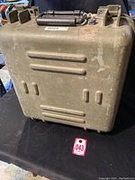 Photo of the closed olive green military-grade plastic carrying case with reinforced corners and handle, showing wear and scratches.