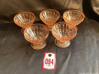 Five pink Depression glass sherbet dessert bowls arranged on a black cloth background, showing the overall set and size.