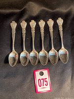 Set of six teaspoons with ornate handles featuring Queen Elizabeth II's coronation portrait and text.