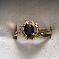 Full front view of ring in display box showing oval sapphire and diamond accent cluster