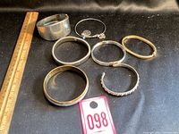 Seven vintage style bracelets arranged on black fabric, showing varied designs and materials.