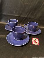 Photo showing 3 blue tea cups on matching saucers set against black background, labeled lot number 012.