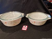 Two vintage Pyrex covered casserole dishes with floral patterns, side by side with lids on