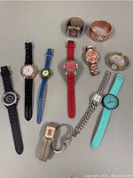 Full lot of 12 wrist watches laid out on white surface showing variety of bands and face shapes