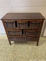 Front view of dark wood dresser with six wicker drawers having leather handles.